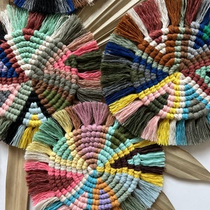 May include: Three colorful round crocheted coasters with fringe. The coasters feature a variety of colors including pink, blue, green, yellow, brown, and white.