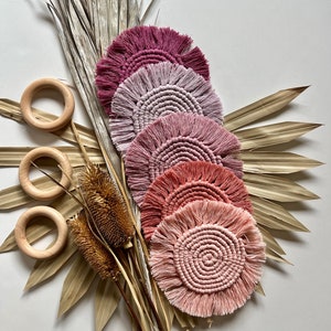 May include: Set of five round crocheted coasters in shades of pink and coral. The coasters have a fringe border and are arranged in a stack.