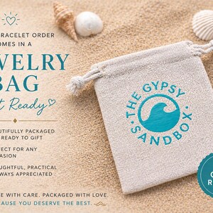 May include: A beige jewelry bag with a drawstring closure, printed with "S. THE GYPSY SANDBOX" and a teal wave logo. The bag is on a sandy surface with seashells and the text "Gift Ready".