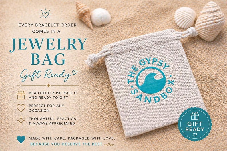 May include: A beige jewelry bag with a drawstring closure, printed with "S. THE GYPSY SANDBOX" and a teal wave logo. The bag is on a sandy surface with seashells and the text "Gift Ready".