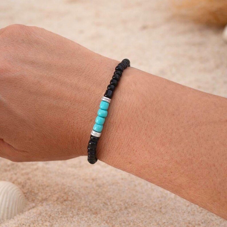 May include: Black beaded bracelet with turquoise and silver accents. The bracelet features small, round black beads interspersed with turquoise beads and silver-colored spacers. The bracelet is worn on a wrist.