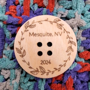 May include: A wooden button with a wreath design, the text "Mesquite, NV" and the year "2024".