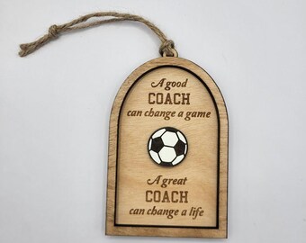 May include: Wooden soccer coach ornament with a jute string for hanging. The ornament has a soccer ball in the center and the text "A good coach can change a game" and "A great coach can change a life".