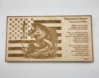 May include: Wooden plaque featuring an American flag design with a bass fish leaping from water, a fishing lure, and the text "Fisherman's Prayer". The plaque is made of light-colored wood and has a natural finish.