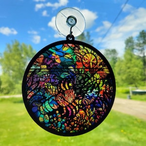 May include: A colourful, stained glass-style car suncatcher with a black frame and a suction cup for hanging. The design features a variety of colours, including red, orange, yellow, green, blue, and purple.