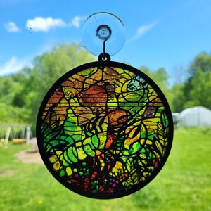 May include: A round, colourful stained glass suncatcher with a black frame. The suncatcher features a variety of colours, including red, orange, yellow, green, and blue. It is designed to hang in a window and catch the light.