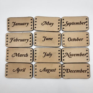 May include: Twelve rectangular leather tags with the months of the year printed on them. Each tag has a row of holes along the top and bottom edges.