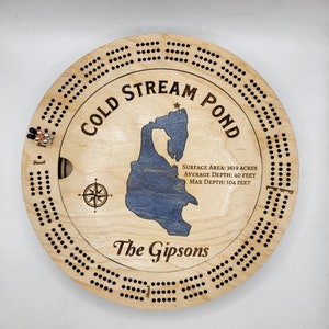 May include: A wooden cribbage board with a map of Cold Stream Pond, featuring the text "Cold Stream Pond", "Surface Area: 3619 Acres", "Average Depth: 40 Feet", "Max Depth: 104 Feet", and "The Gipsons".
