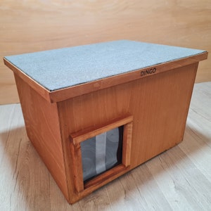 May include: A wooden dog house with a gray roof and a small window. The house is labeled "DINGO" on the roof.