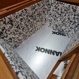 May include: The inside of a wooden box lined with white foam insulation. The foam has a speckled pattern and the word "LANNOK" is printed on it in green letters.