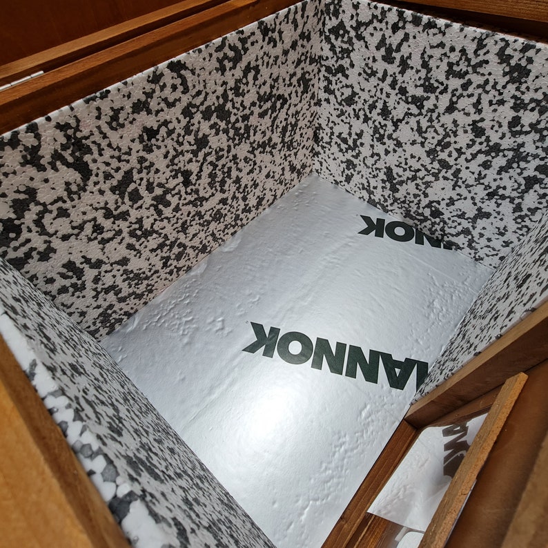 May include: The inside of a wooden box lined with white foam insulation. The foam has a speckled pattern and the word "LANNOK" is printed on it in green letters.