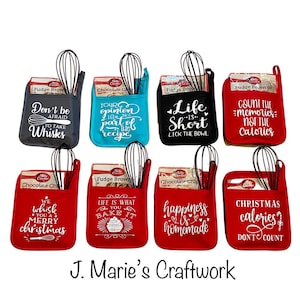 May include: Set of eight red, blue, black, and gray oven mitts with white text and a whisk. The mitts feature various sayings, including "Don't be afraid to take whisks", "Your opinion is not part of the recipe", "Life is short, lick the bowl", "Count the memories, not the calories", "We whisk you a merry christmas", "Life is what you bake it", "Happiness is homemade", and "Christmas calories? Don't count".