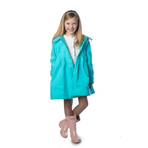 May include: A young girl wearing a turquoise raincoat and pink rain boots. She is smiling and looking at the camera.