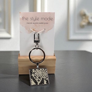 May include: A keychain with a square pendant featuring a snakeskin pattern in black and cream. The keychain has a silver-tone metal ring and clasp. The product is displayed on a card that reads "the style mode HAND MADE EARRINGS".