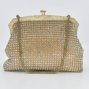 May include: A vintage gold evening bag with a chain strap. The bag is covered in sparkling rhinestones, with a gold-toned frame and clasp. The interior appears to be a light orange fabric. A classic accessory for special occasions.