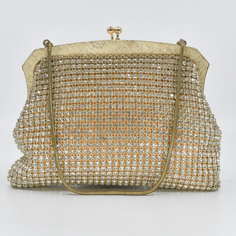 May include: A vintage gold evening bag with a chain strap. The bag is covered in sparkling rhinestones, with a gold-toned frame and clasp. The interior appears to be a light orange fabric. A classic accessory for special occasions.