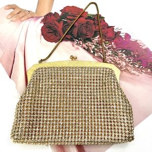 May include: A vintage gold-toned evening bag with a delicate chain handle. The bag is covered in a shimmering, textured pattern. The clasp is a small, decorative gold tone. The background includes a bouquet of red roses.