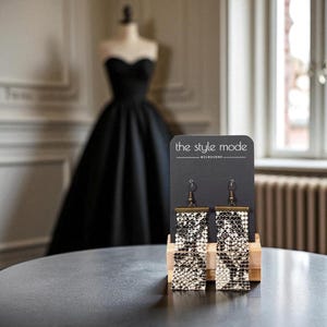 May include: Rectangular earrings with a monochrome pattern, presented on a black card with the text "the style mode MELBOURNE". The earrings are displayed on a wooden stand, with a black dress visible in the background.