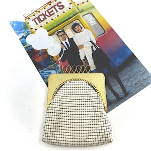 May include: A vintage gold-toned metal mesh purse with a rectangular frame and a rounded top. The purse features a delicate chain detail around the frame and a white mesh body. A colorful vintage-style illustration is in the background.