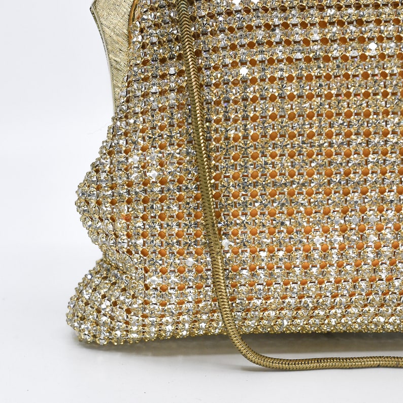 May include: A vintage gold evening bag with a chain strap. The bag is covered in sparkling rhinestones, creating a shimmering effect. The interior appears to be a warm, golden color. The bag's design is classic and elegant, suitable for formal events.