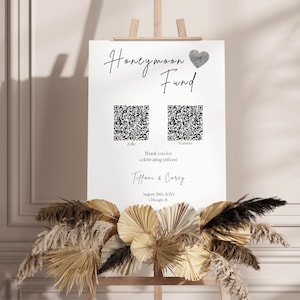 Könnte beinhalten: Ein weißes Schild mit schwarzem Text, der "Honeymoon Fund" lautet, mit einem schwarzen Herzen und zwei QR-Codes. Der Text unter den QR-Codes lautet "Vielen Dank, dass Sie mit uns feiern!" gefolgt von den Namen "Tiffany & Corey" und dem Datum "20. August 20XX, Chicago, IL."