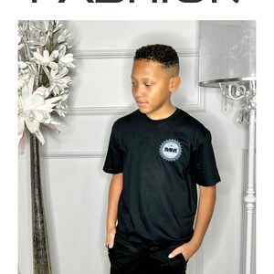K&ouml;nnte beinhalten: Schwarzes T-Shirt mit einem grauen und wei&szlig;en Logo, auf dem "MM" in einem Kreis steht. Das Shirt wird mit schwarzen Shorts kombiniert. Das Model tr&auml;gt ein schwarzes T-Shirt und schwarze Shorts. Gr&ouml;&szlig;e: Small.