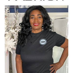 K&ouml;nnte beinhalten: Schwarzes T-Shirt mit kurzen &Auml;rmeln und einem grauen Logo mit der Aufschrift "MM" in einem Kreis. Das T-Shirt wird von einer Person mit dunklen Haaren und einem L&auml;cheln getragen. Der Text "SIZE: LARGE" befindet sich am unteren Rand des Bildes.