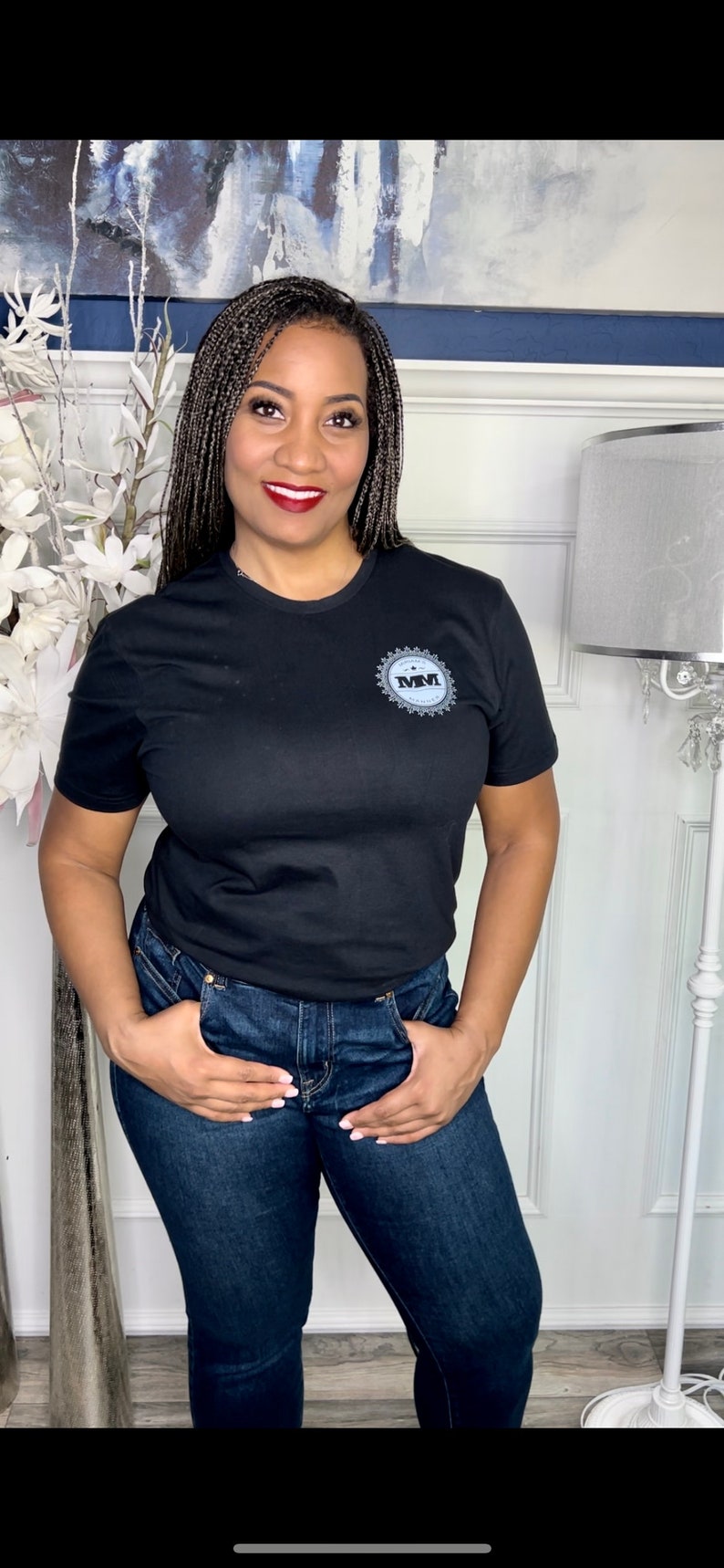 K&ouml;nnte beinhalten: Eine Frau tr&auml;gt ein schwarzes T-Shirt mit einem grauen Logo, auf dem "MMVI" steht, und blaue Jeans.