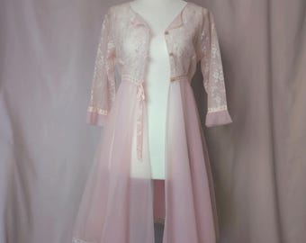 Op de afbeelding: Een vintage roze lingerieset op een mannequin. De set bevat een doorschijnende, lange ochtendjas met kanten rand en een bijpassend kanten jasje met driekwart mouwen. De ochtendjas heeft een strik in de taille.