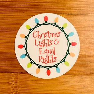 May include: A white round sticker with a green wreath of colorful Christmas lights and the text "Christmas Lights & Equal Rights".