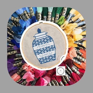 May include: A blue and white cross-stitch embroidery of a Chinese ginger jar with a floral design. The embroidery is framed in a wooden hoop and surrounded by colorful embroidery floss.