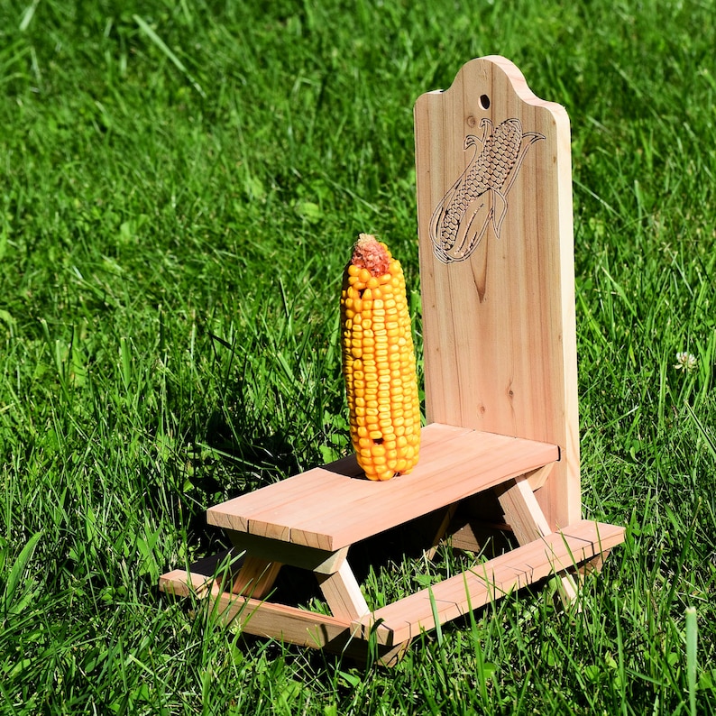A corn cob squirrel feeder shaped like a picnic table sitting in the grass.