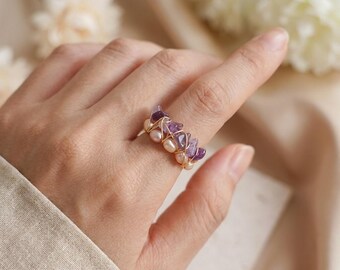 May include: A gold wire ring featuring a cluster of purple amethyst stones and small, round pearls. The ring is designed with a delicate wire wrapping, showcasing the natural beauty of the gemstones. The ring is a piece of jewelry.