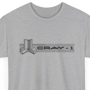 May include: A heather grey t-shirt featuring a dark grey graphic of the Cray-1 supercomputer. The design includes the text CRAY-1, WORLD'S FASTEST SUPERCOMPUTER | 1976-1982, 64-BIT VECTOR PROCESSOR | 80MHZ | 8MB RAM | 160 MFLOPS printed in a clean font.