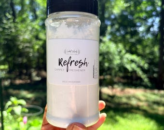May include: A clear plastic shaker bottle with a black lid containing white carpet freshener powder. The white label features the text Refresh Carpet Freshener and 16oz/453grams. The bottle has a cylindrical shape and a wide opening for dispensing.