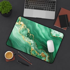 May include: A rectangular mousepad with a green and gold marble design. The mousepad has a black border and a white computer mouse is on top. A laptop, coffee cup, and notebooks are also visible.