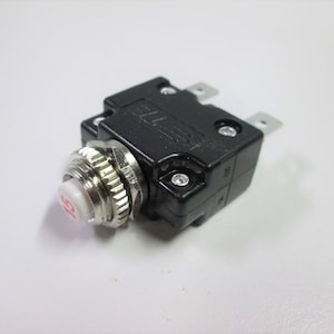 May include: A black circuit breaker with a white reset button. The button has a red number "15" printed on it.