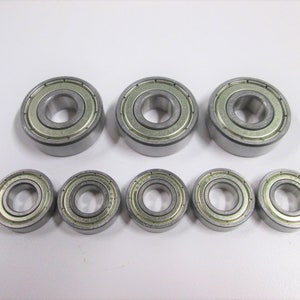 May include: A set of eight silver ball bearings of various sizes. The bearings are arranged in two rows, with the larger bearings in the front and the smaller bearings in the back.