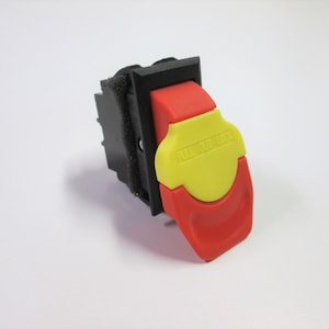May include: A red and yellow safety switch with a black housing. The switch has a pull-out lock feature and the text "PULL OUT TO LOCK" is printed on the yellow portion of the switch.