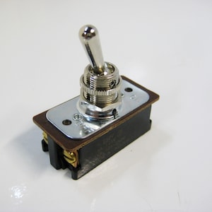 May include: A silver toggle switch with a black base and a brown plastic plate. The switch has a lever that can be flipped to turn it on or off.
