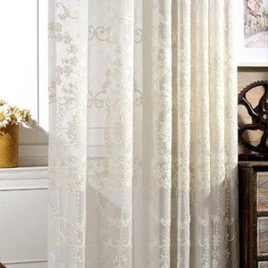 May include: White sheer curtains with an embroidered floral pattern. The curtains are hanging in a window and are letting in natural light.