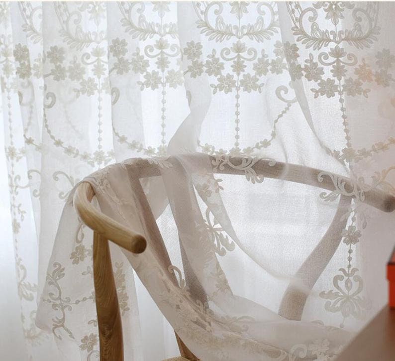 May include: White sheer curtains with delicate floral embroidery. The curtains are draped over a wooden chair.