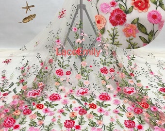 May include: White floral embroidered tulle fabric with pink, red, and orange flowers. The fabric is sheer and delicate, with a soft, flowing texture.