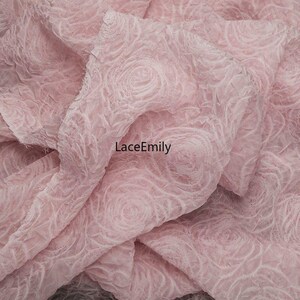 Puede incluir: Tela rosa p&aacute;lido con un patr&oacute;n de rosas. La tela tiene un aspecto texturizado y tridimensional, con el dise&ntilde;o de rosas ligeramente en relieve. La tela est&aacute; doblada, creando sombras. El texto "LaceEmily" es visible.