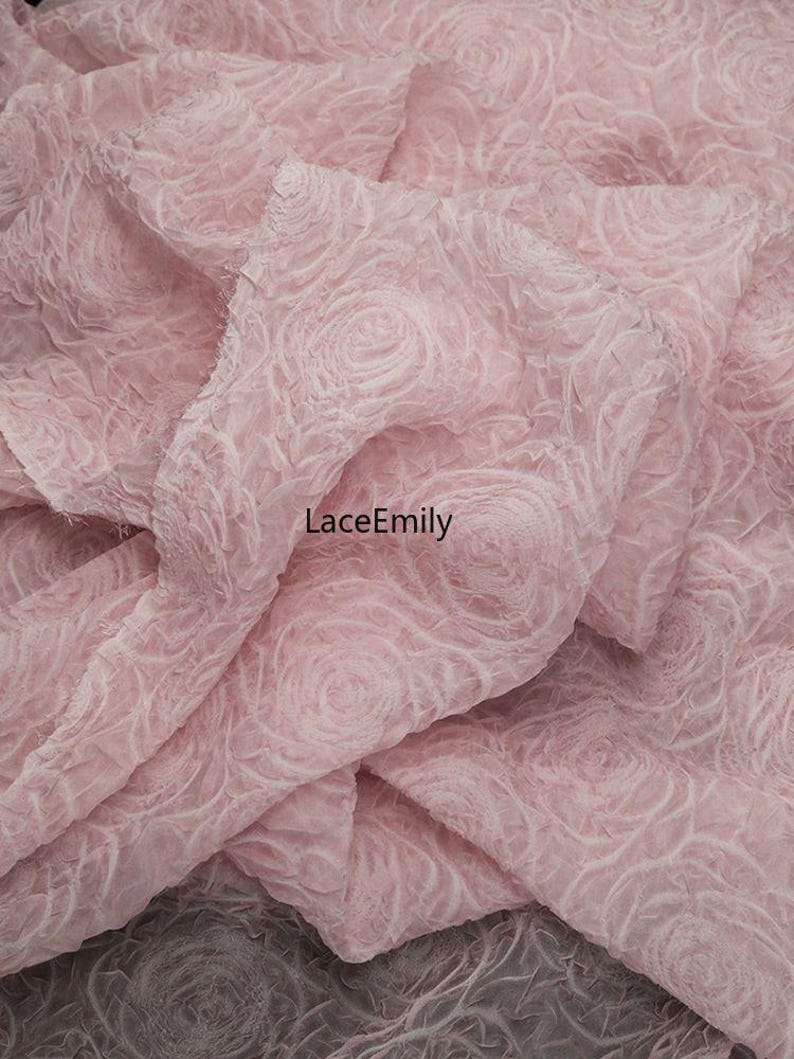 Puede incluir: Tela rosa p&aacute;lido con un patr&oacute;n de rosas. La tela tiene un aspecto texturizado y tridimensional, con el dise&ntilde;o de rosas ligeramente en relieve. La tela est&aacute; doblada, creando sombras. El texto "LaceEmily" es visible.