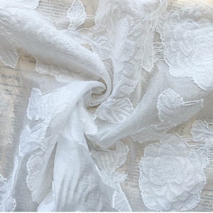 Puede incluir: Tela blanca transparente con un patr&oacute;n floral en relieve. La tela es delicada y tiene una textura suave y fluida.