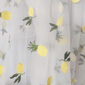 Puede incluir: Tela blanca transparente con piñas y limones amarillos bordados. La tela tiene un tacto delicado y aireado.