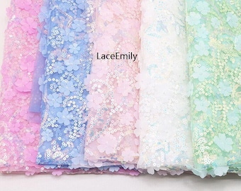Puede incluir: Cinco rollos de tela con estampado floral iridiscente en rosa, azul claro, blanco y verde claro. La tela está hecha de una malla transparente con lentejuelas.