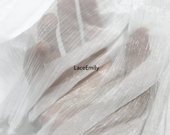 Puede incluir: Una tela blanca, plisada y transparente con un acabado ligeramente brillante. El material es ligero y traslúcido, permitiendo ver a través de los pliegues. El texto LaceEmily está impreso en negro en el centro de la tela.