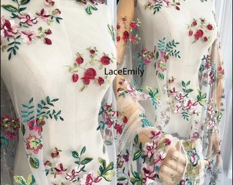 May include: White tulle fabric with embroidered floral designs in shades of pink, red, and green. The fabric is sheer and delicate, with a soft, flowing texture.